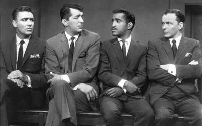 Peter Lawford, Dean Martin, Sammy Davis Jr, and Frank Sinatra sitting on a bench talking 