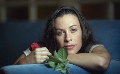 Alanis Morissette poses on the couch with a rose in her hand. 
